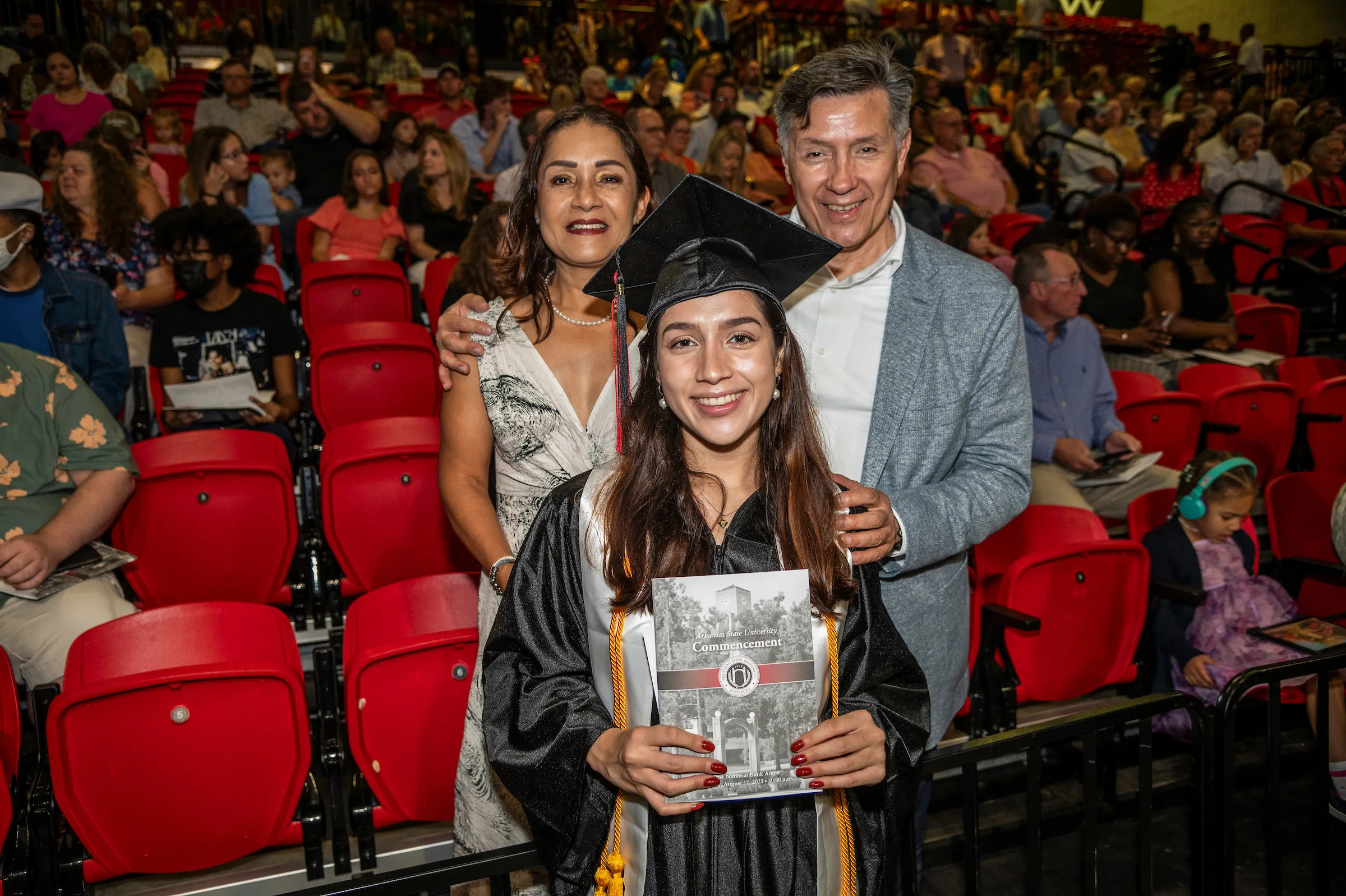 A smiling grad poses for a photo with her parents