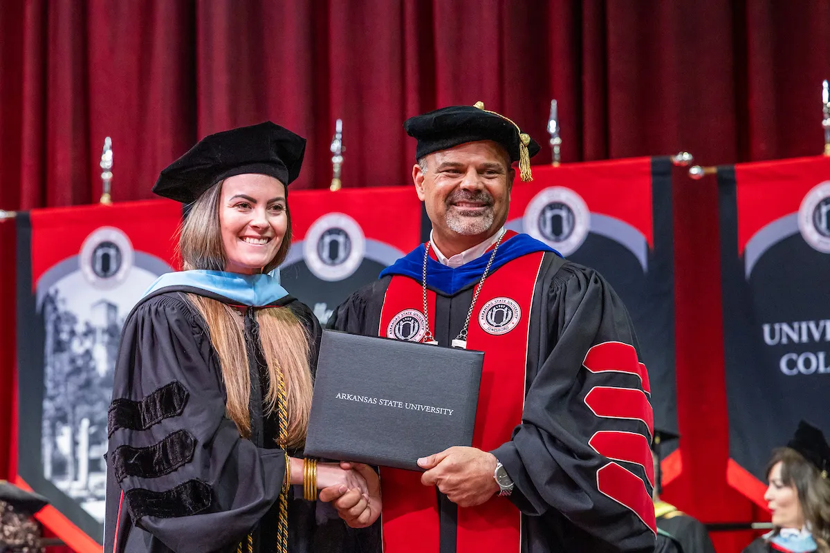 A student receives her diploma from Chancellor Todd Shields