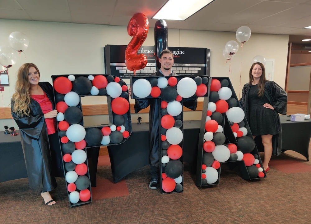 Physical Therapy Assistant students standing next to large PTA sign filled with balloons after graduation.