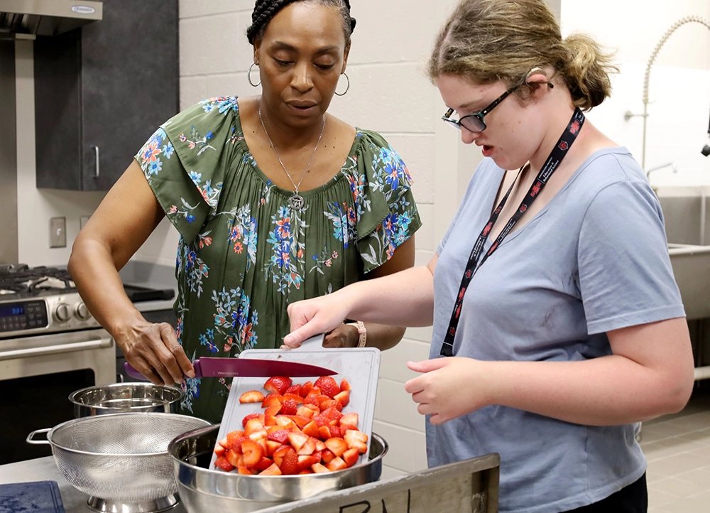 Teacher teaching H.O.W.L. student how to cut fruit.