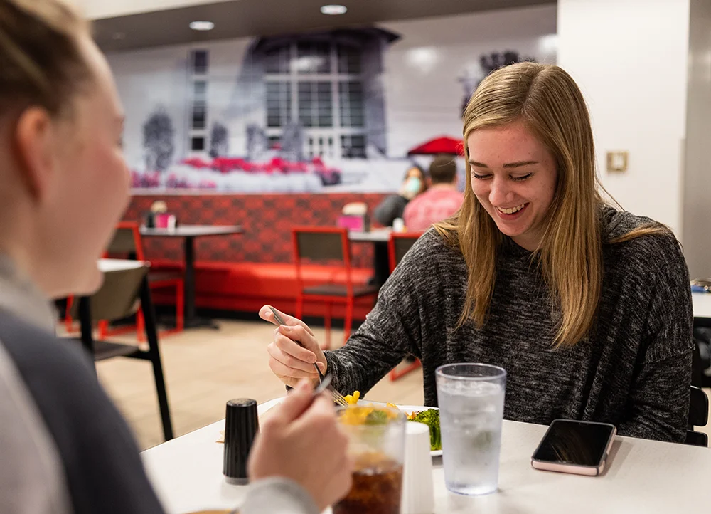 A smiling student eating in the Acansa Dining Hall.