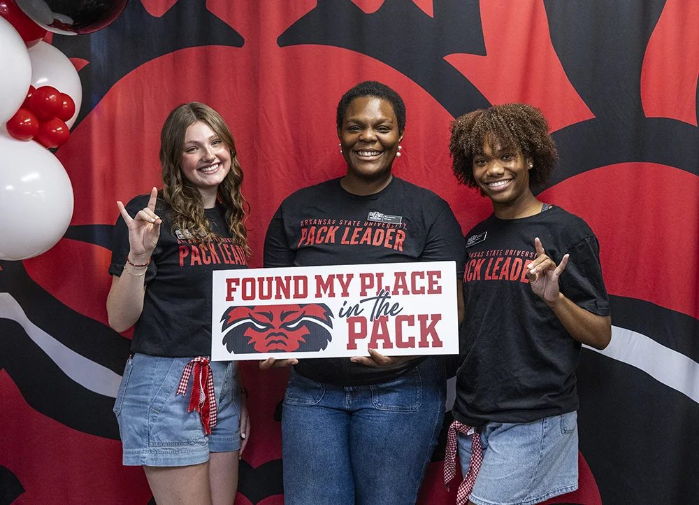 Three students posing with a sign.