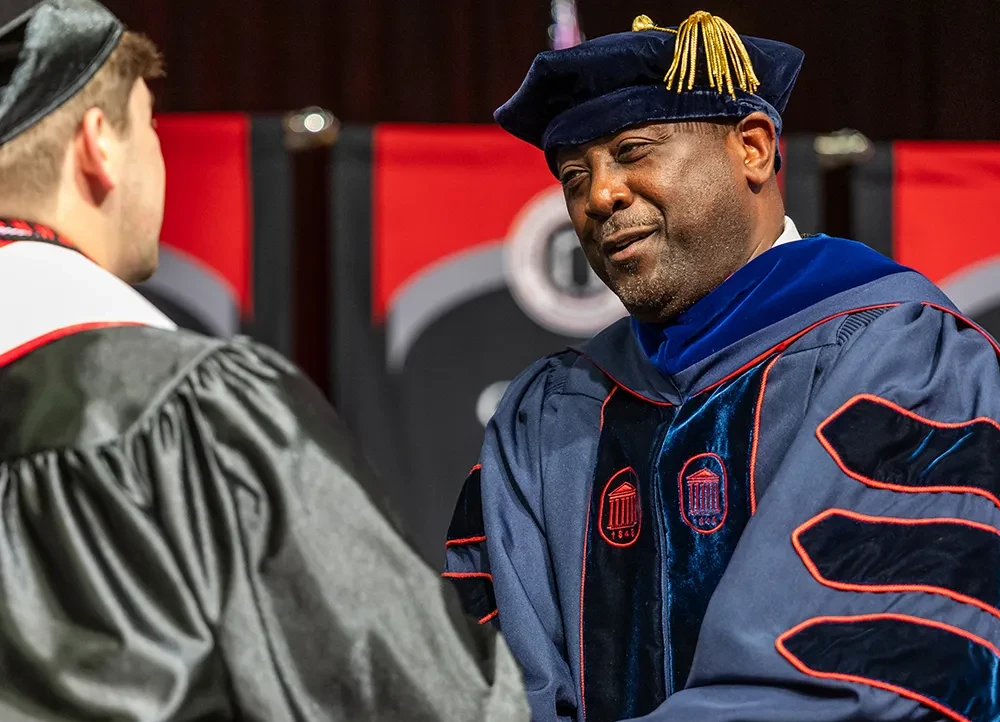 Dr. Calvin White shakes a student's hand at a commencement ceremony.