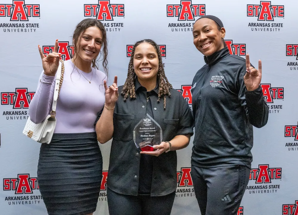 3 people posing for leadership award at the excellence awards ceremony, giving the wolves up sign.