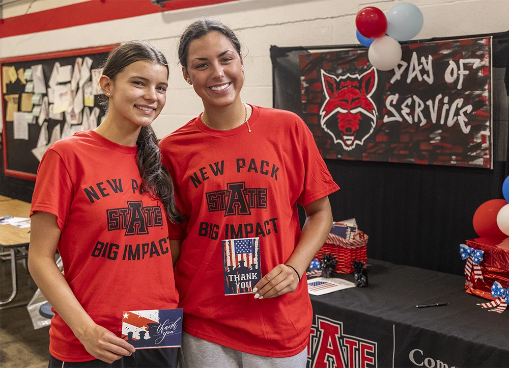 Two students smile at the camera in front of a "Freshmen Day of Service" banner.