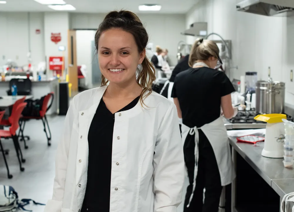 Nutrition student in kitchen area smiling for picture with lab coat on