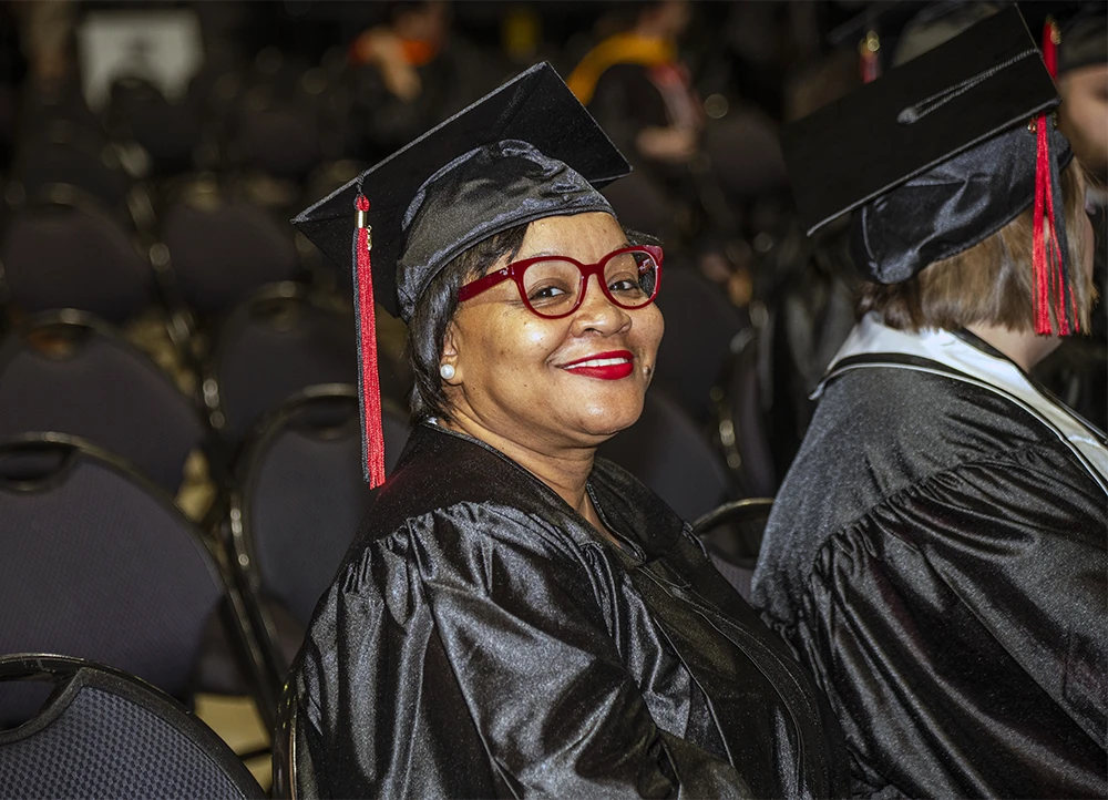 Older graduate smiles at camera in cap and gown.