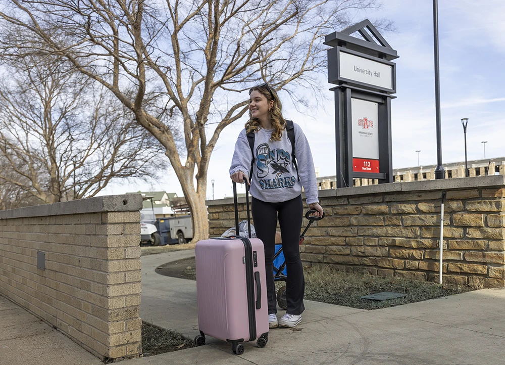 Student moving into University Hall with a suitcase.