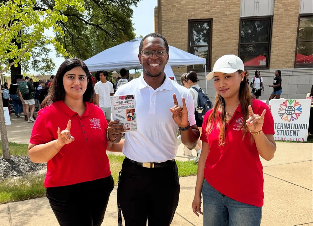 Three CLE members giving Wolves Up on campus.