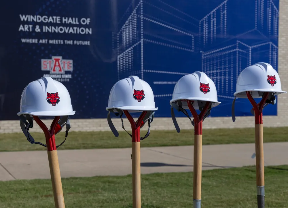 a-state hard hats on shovels sticking into the ground with the windgate construction behind it.