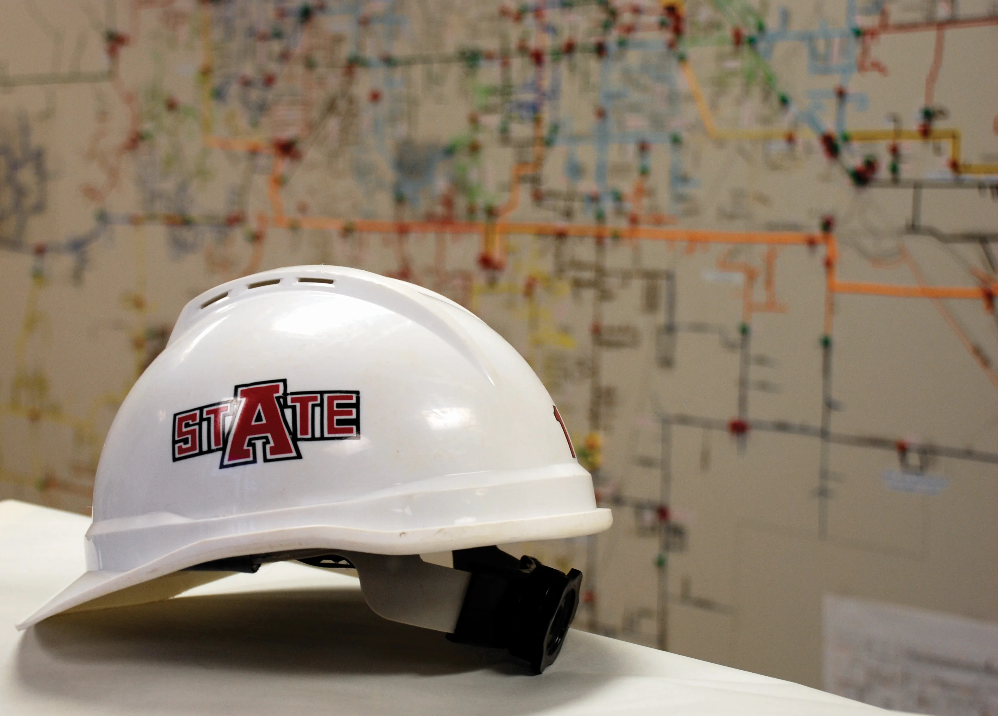 A-State hard hat with blurry city infrastructure map background.