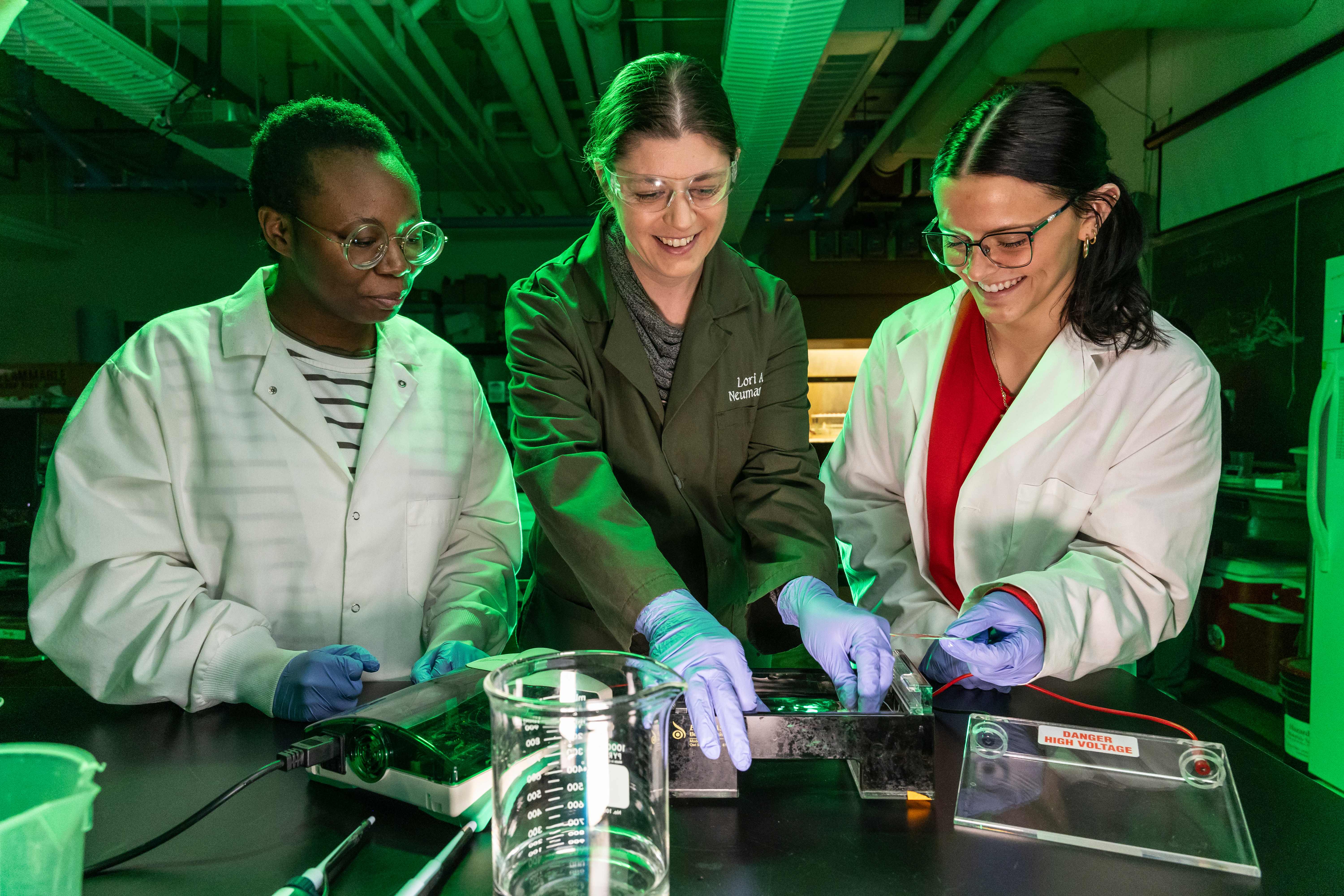 A professor and two students smiling together as they do an experiment.