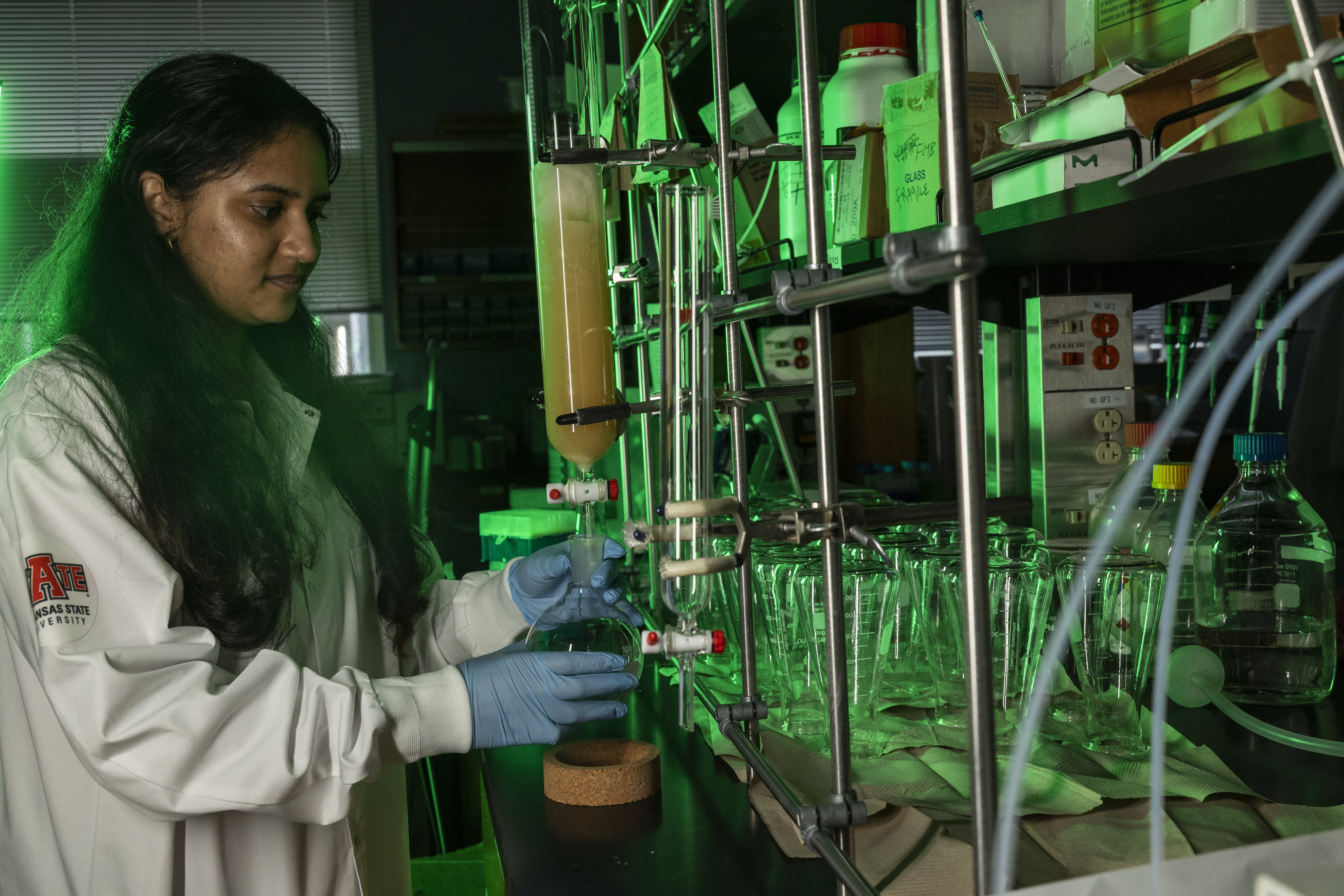A student wearing a lab coat with the A-State logo on it performing an experiment with a beaker.