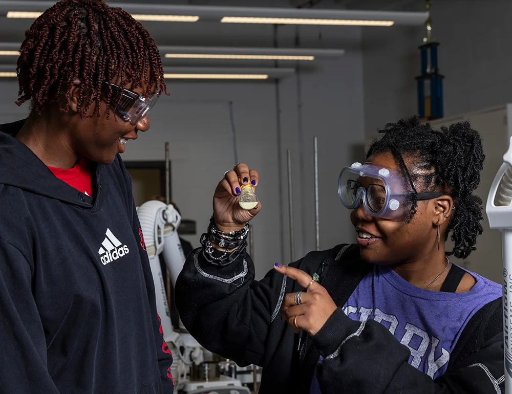 Two students smiling as they inspect a beaker.