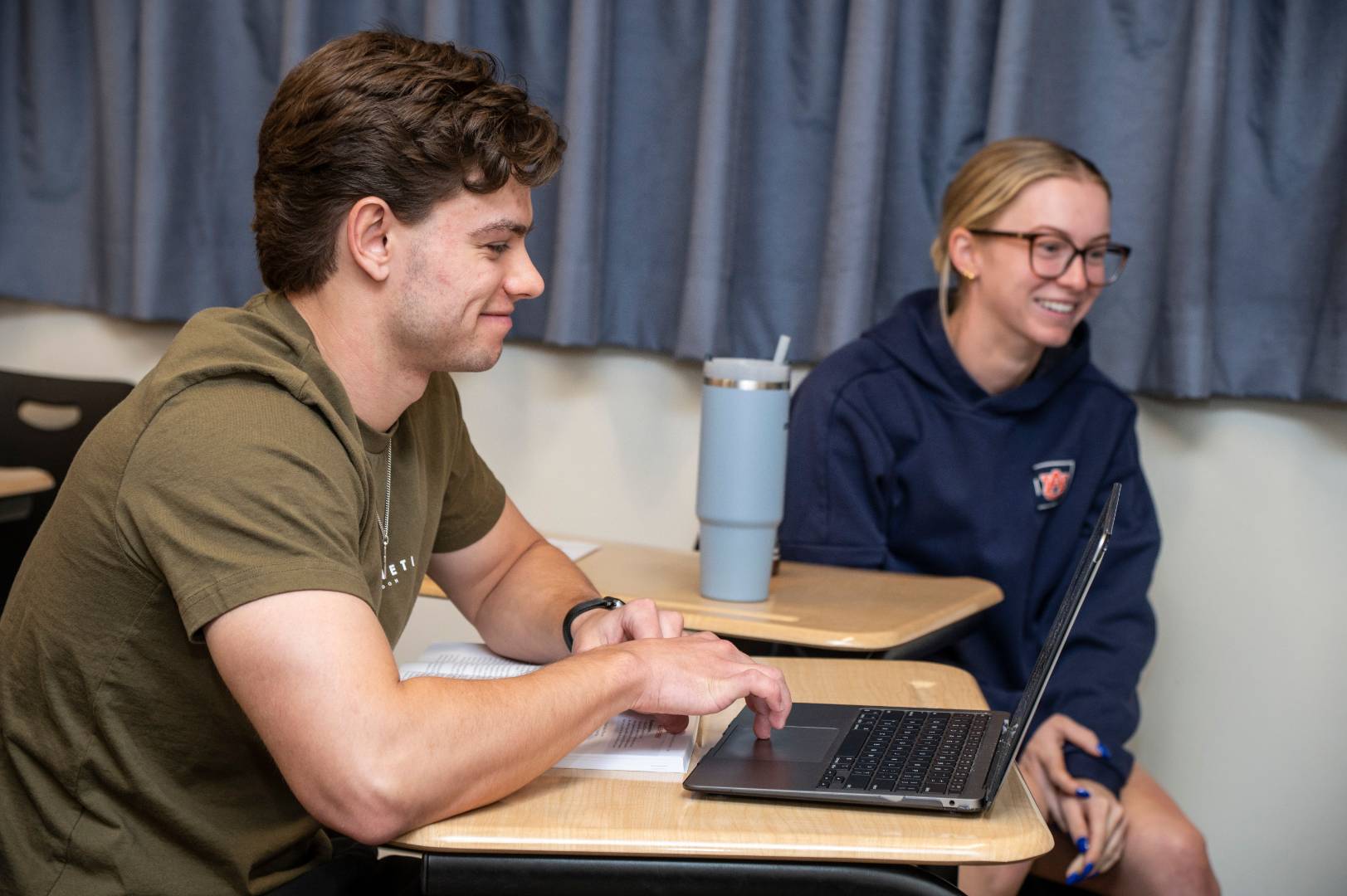 Two students sitting at desks and smiling.