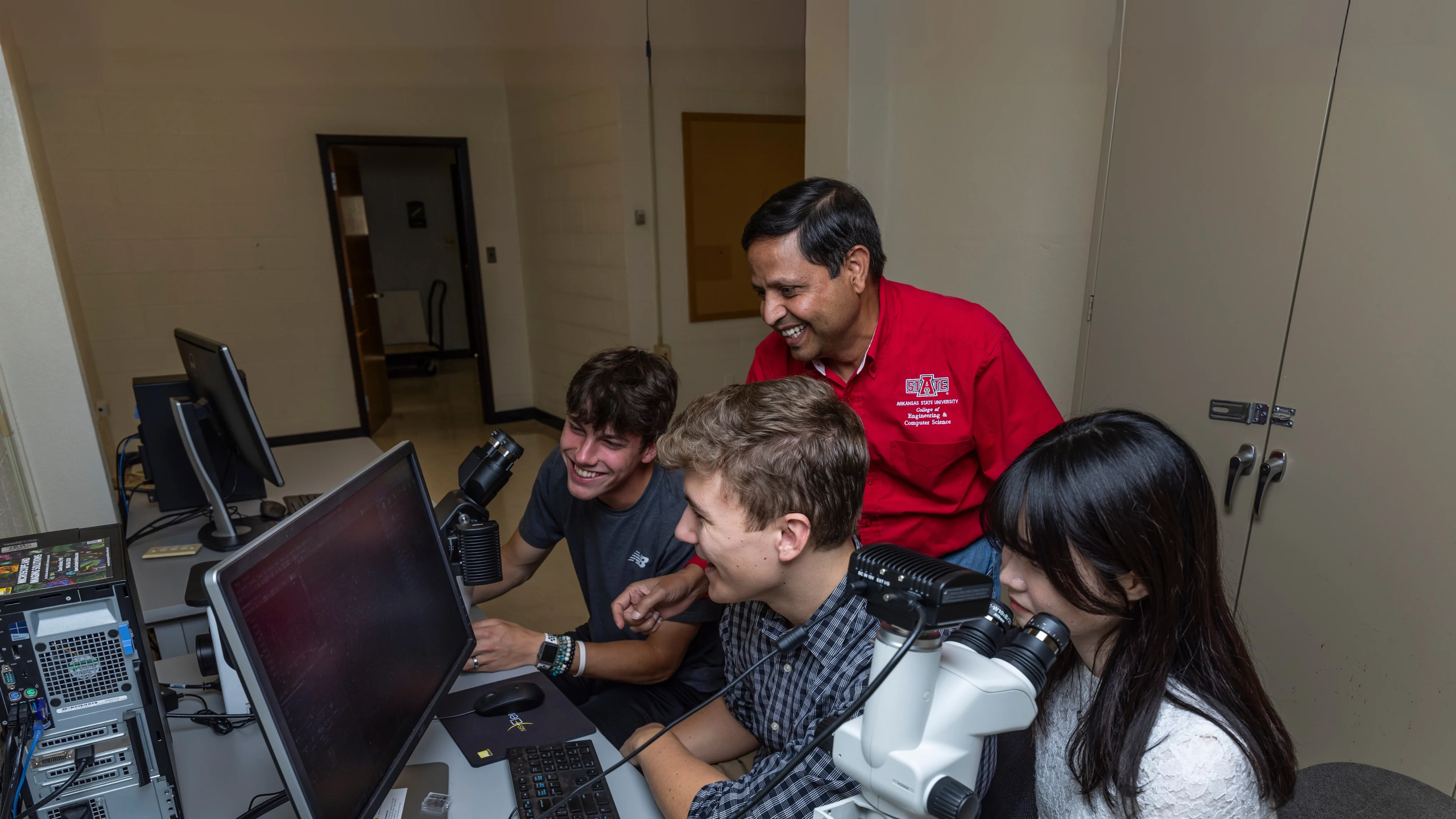 Engineering professor teaching students at a computer while they all laugh.
