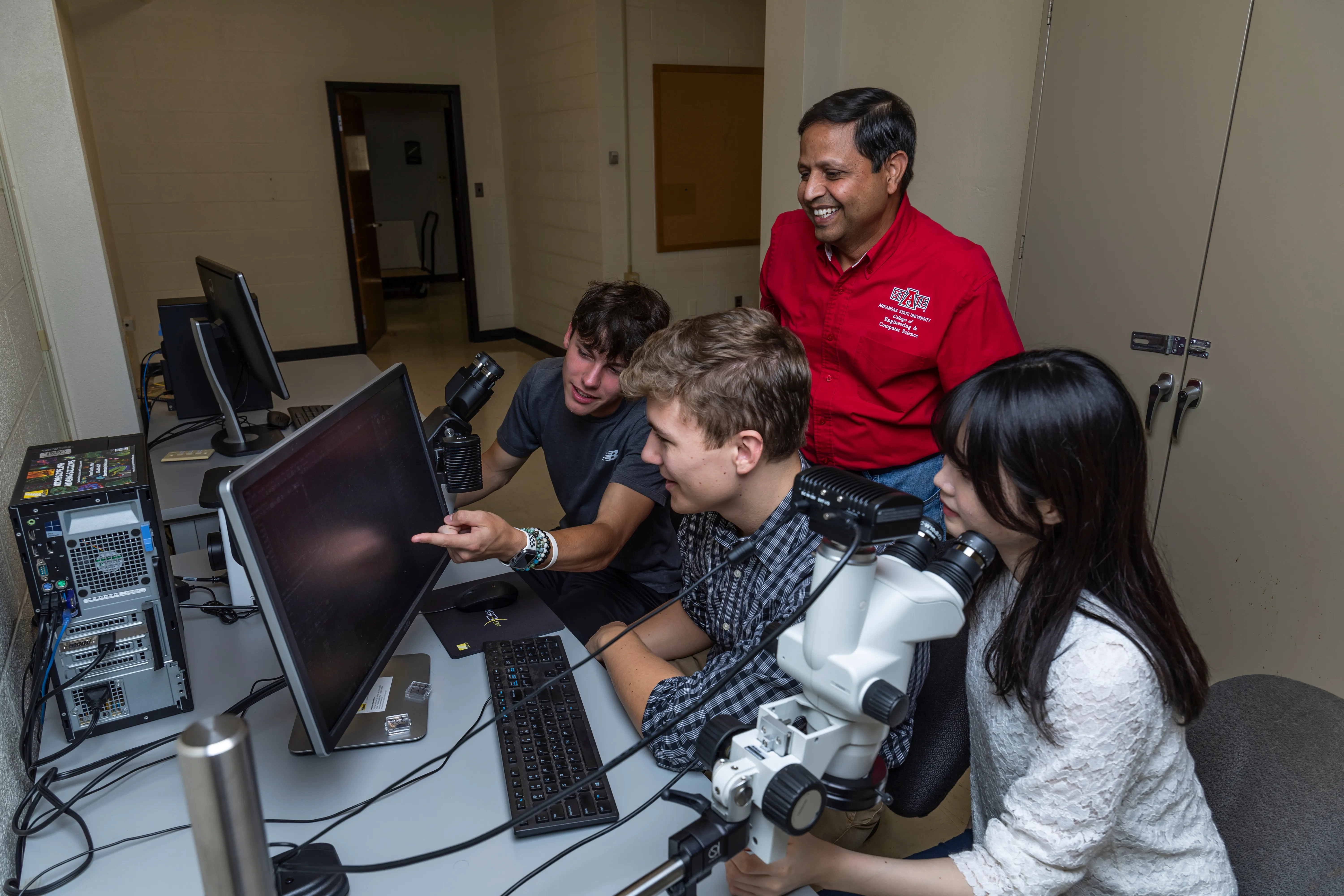 engineering technology students with  dr. sharma going over labs with a microscope.