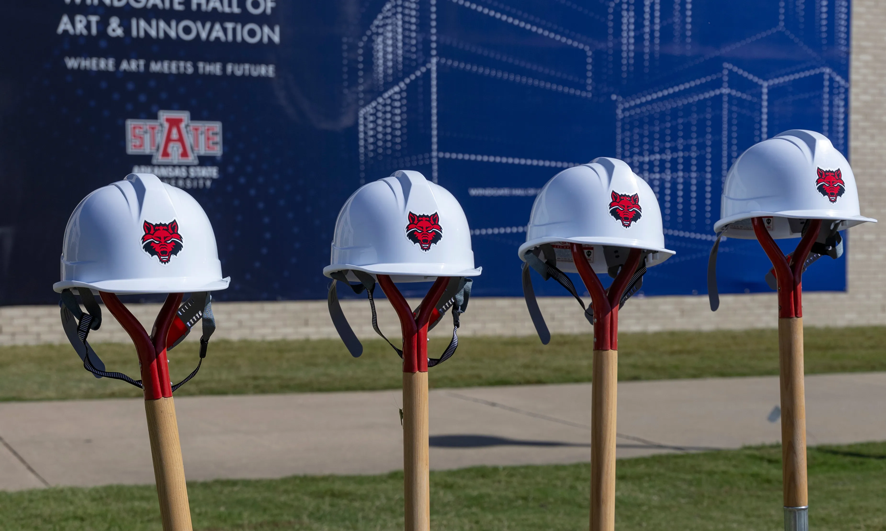 A-State hard hats lined up on top of shovels in the ground at the groundbreaking site of a new building on campus.