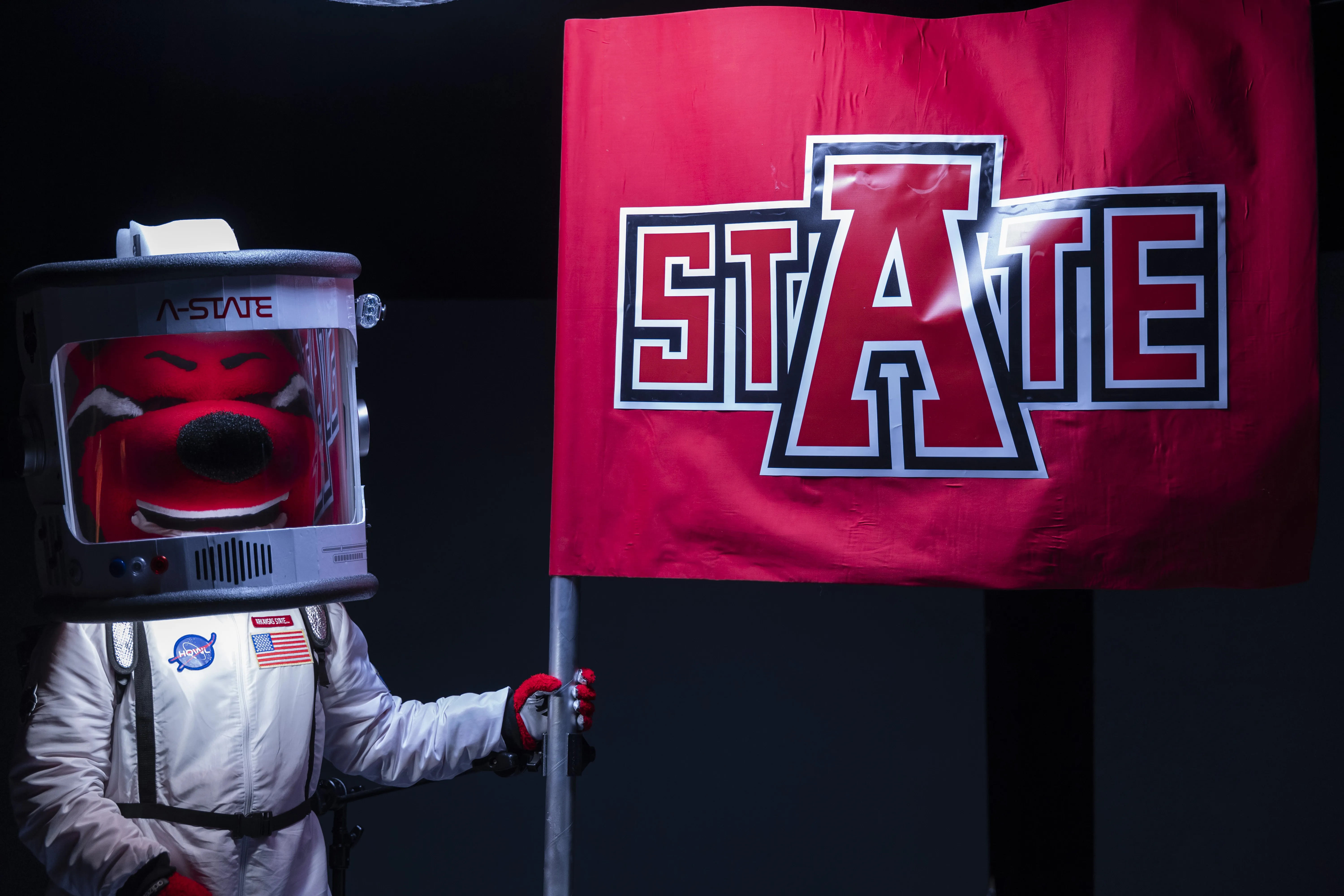 Howl mascot in a space suit holding A-State flag