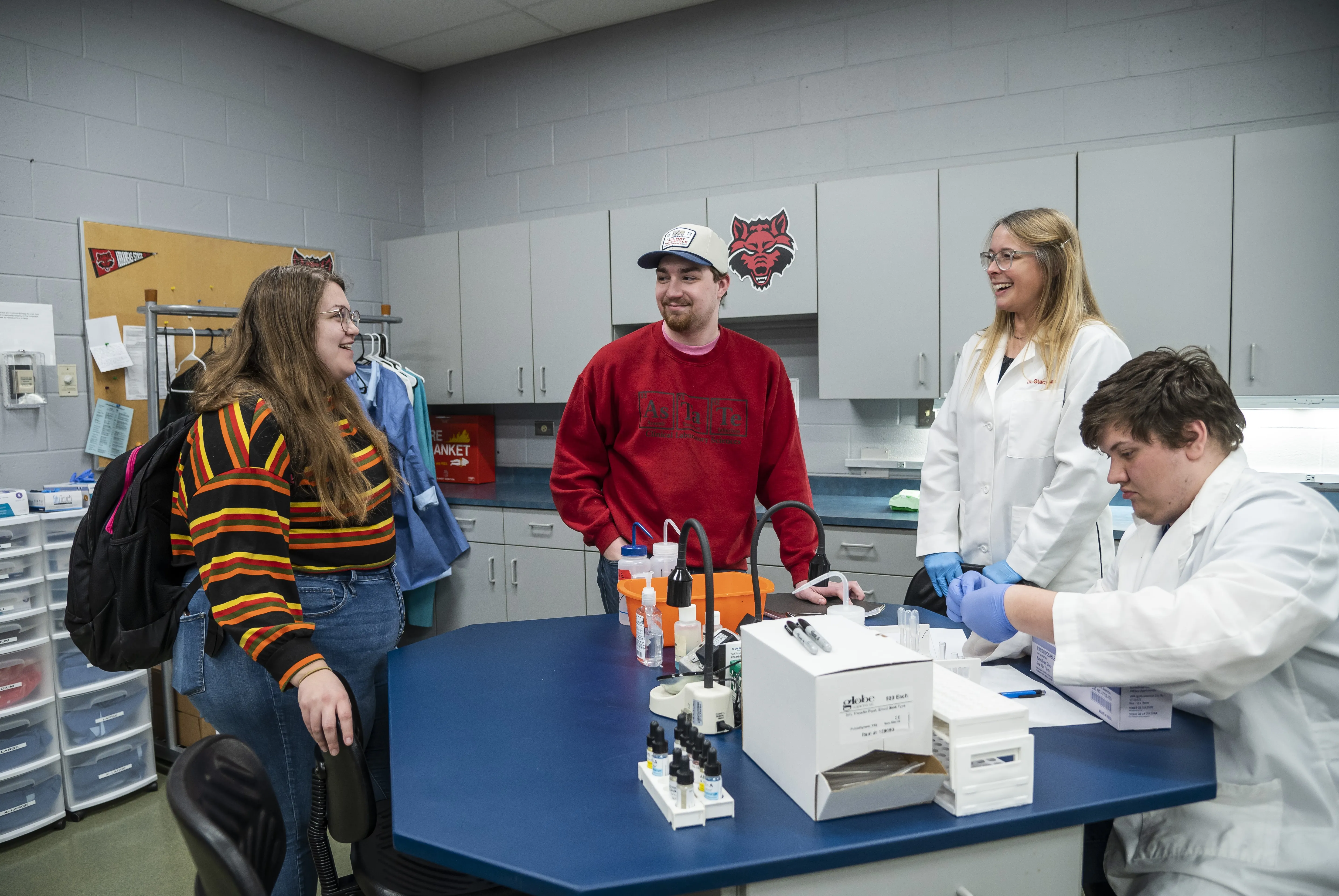 Clinical Lab student looking at sample with teacher and students laughing in conversation.