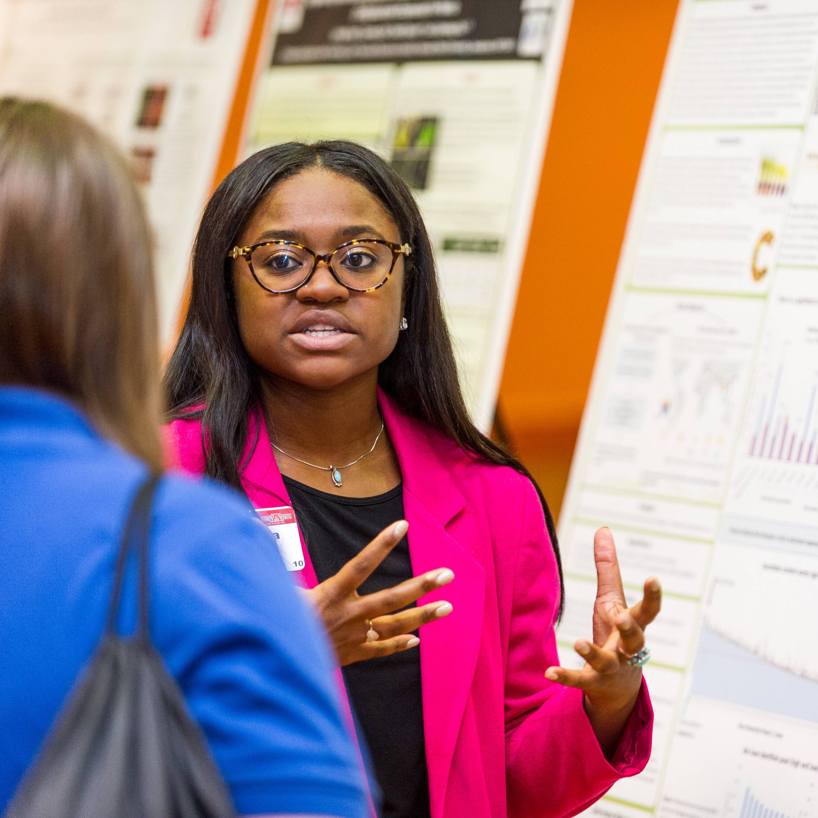 Person talking to someone in the foreground about a project poster pinned to the wall