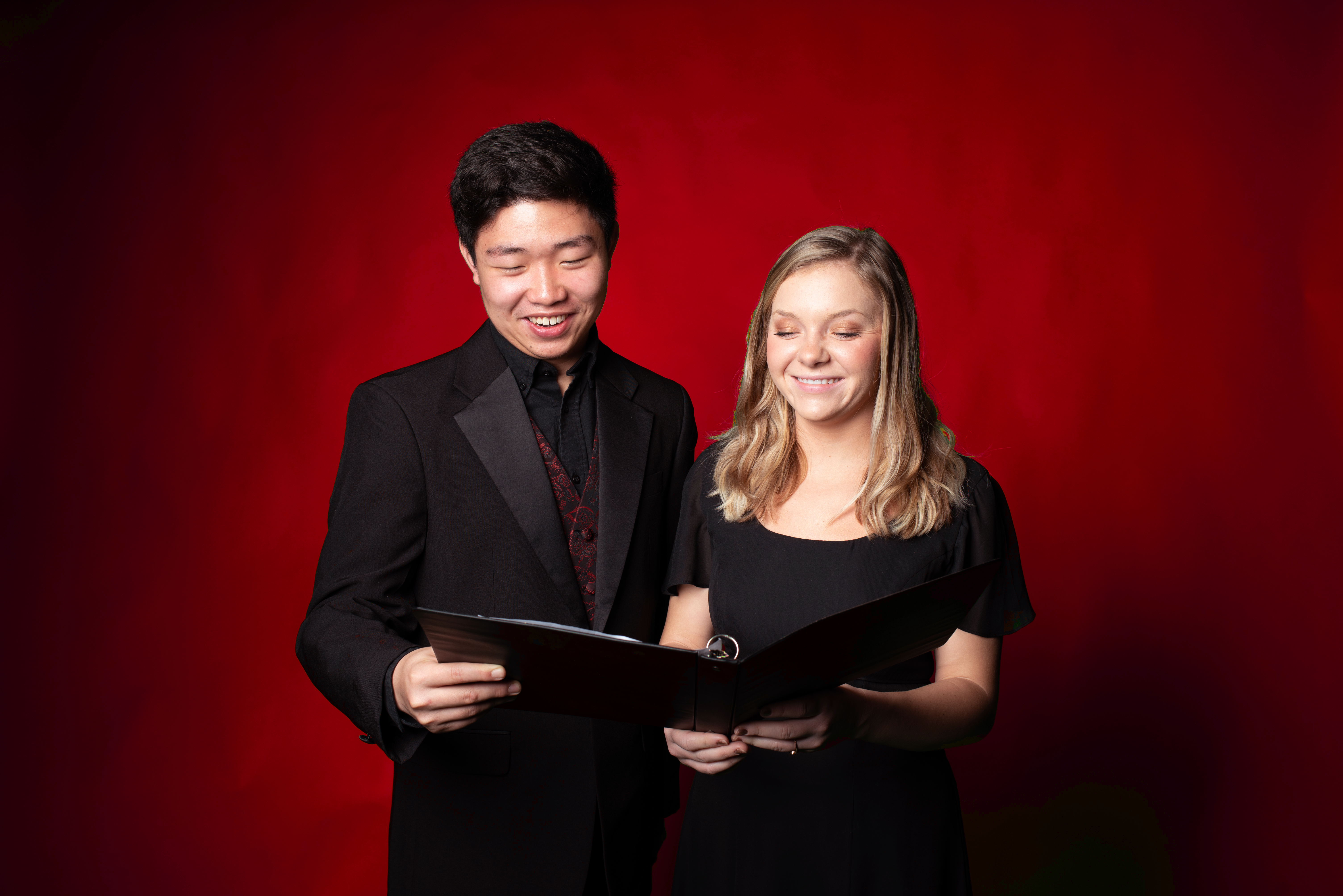 Two students sharing a choir book and smiling.