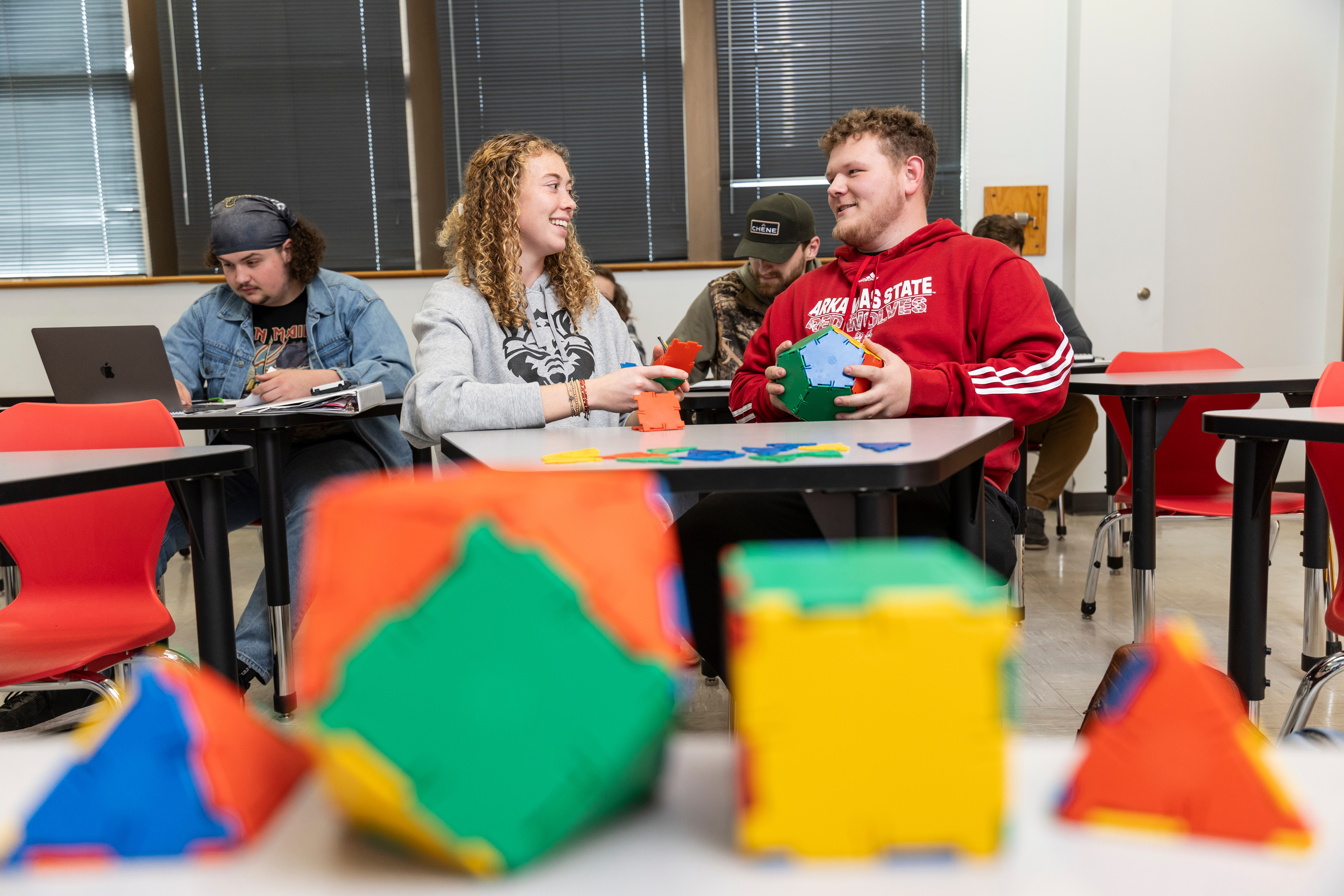 Two students talk as they work with 3D models for a math project.