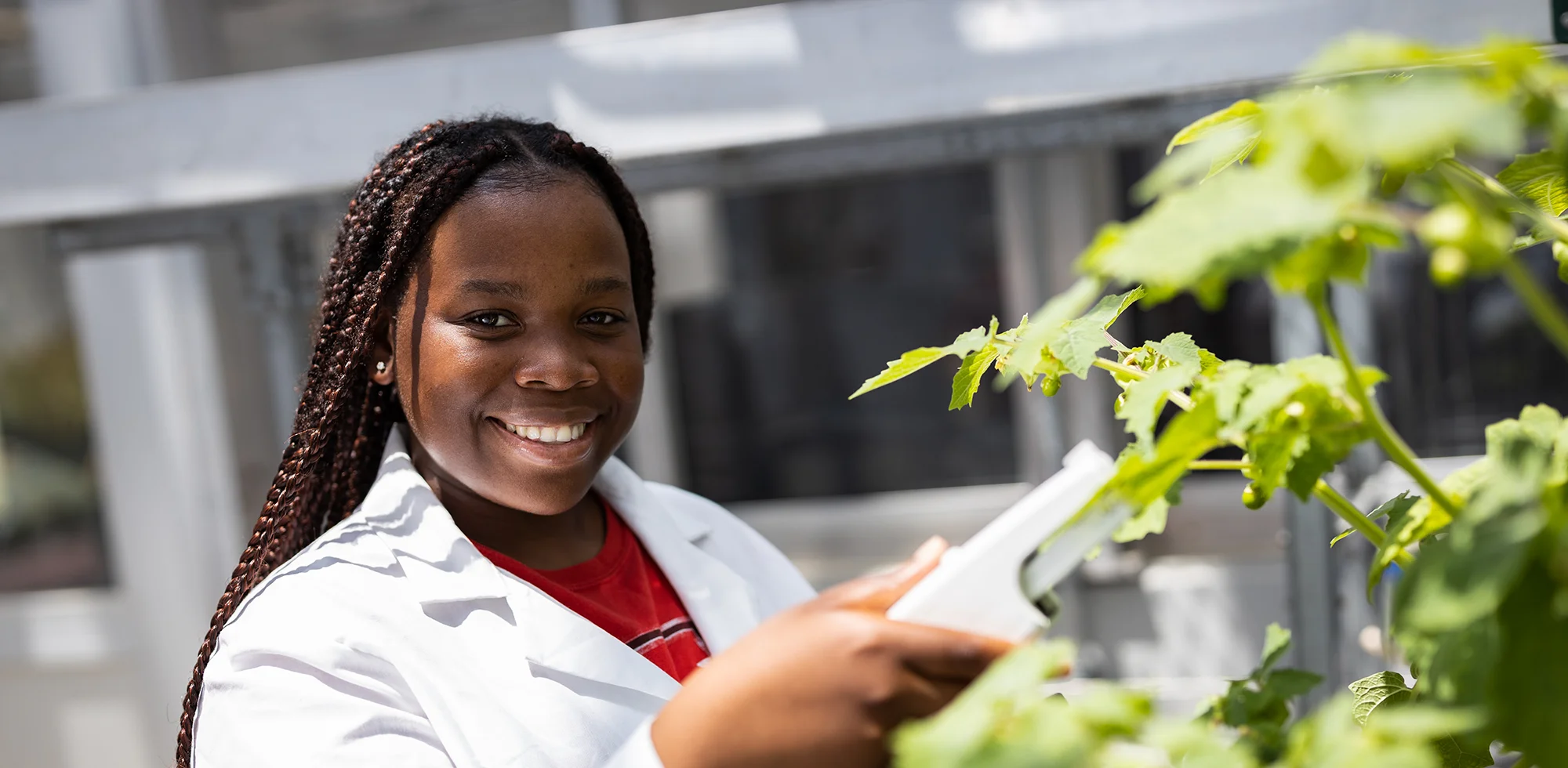 A student smiling as she performs an experiment on a plant.