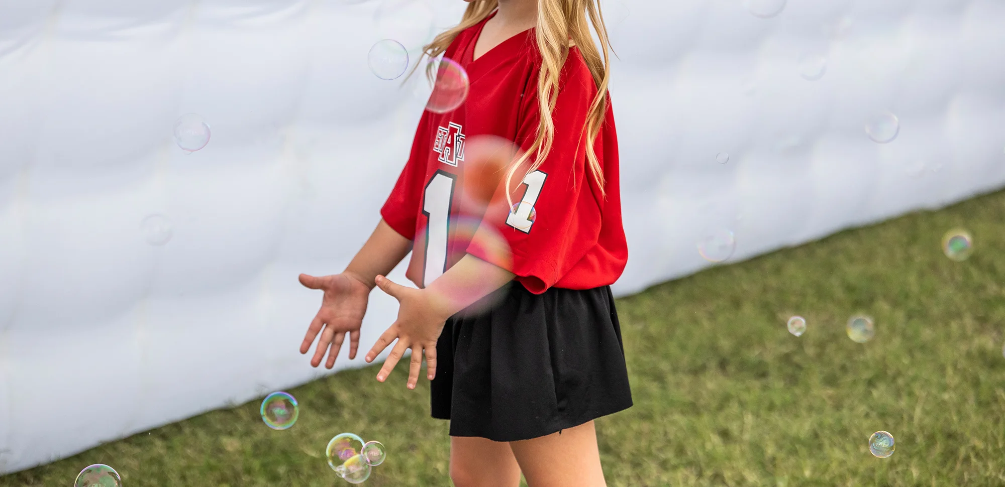 A child in A-State gear playing with bubbles with her face obscured.