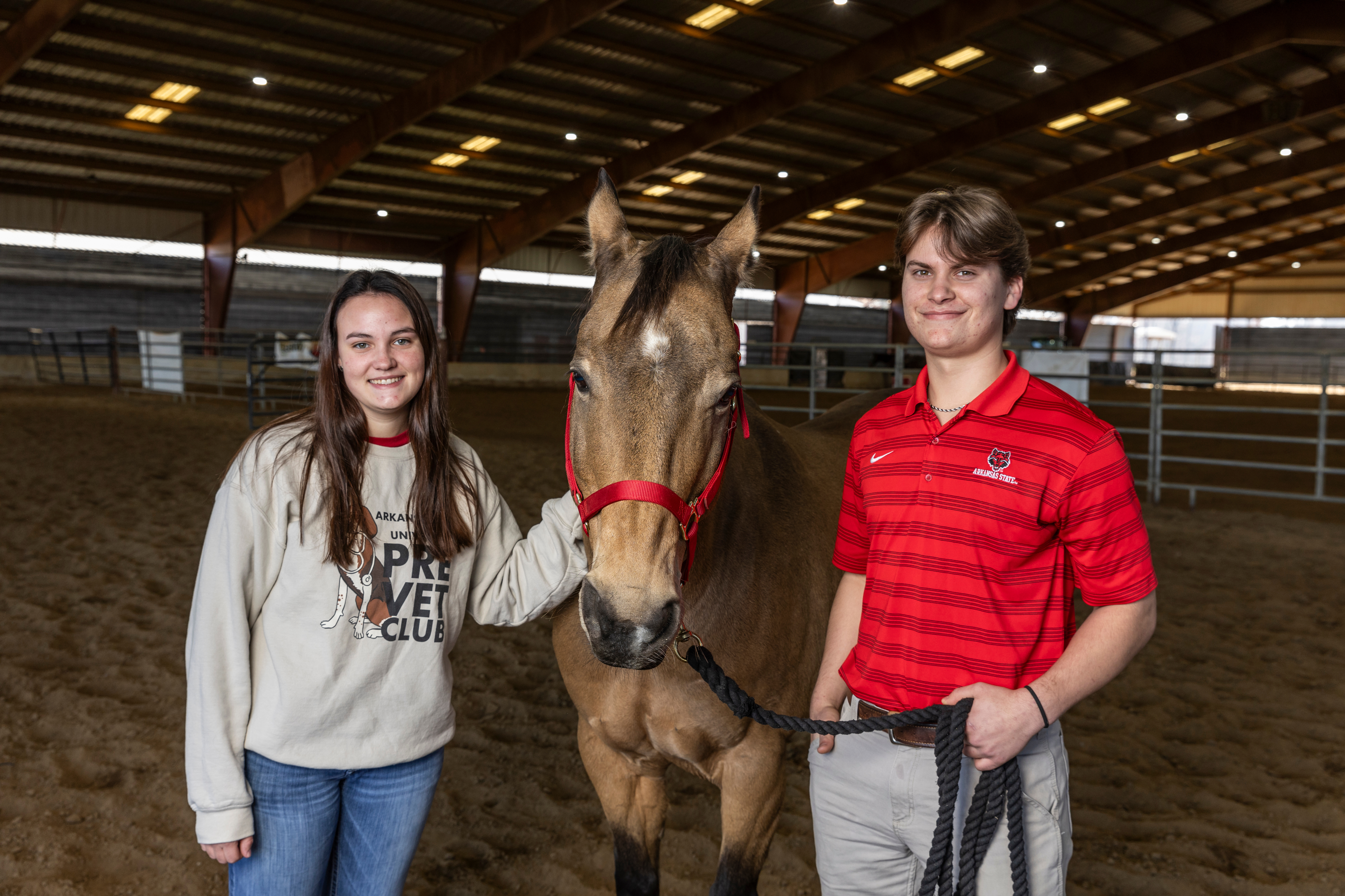 Two Pre-Vet students smiling and standing next to a brown horse.