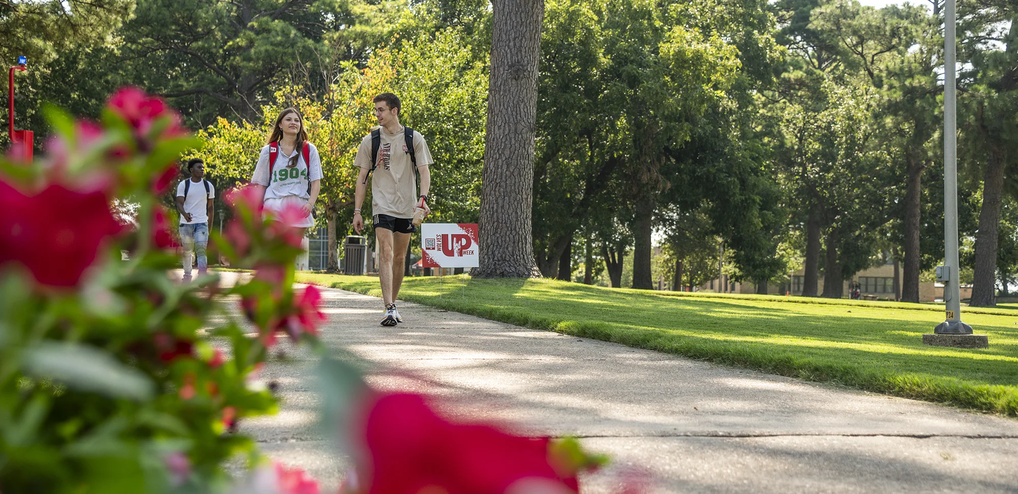 Two students walking on campus, framed by red flowers.