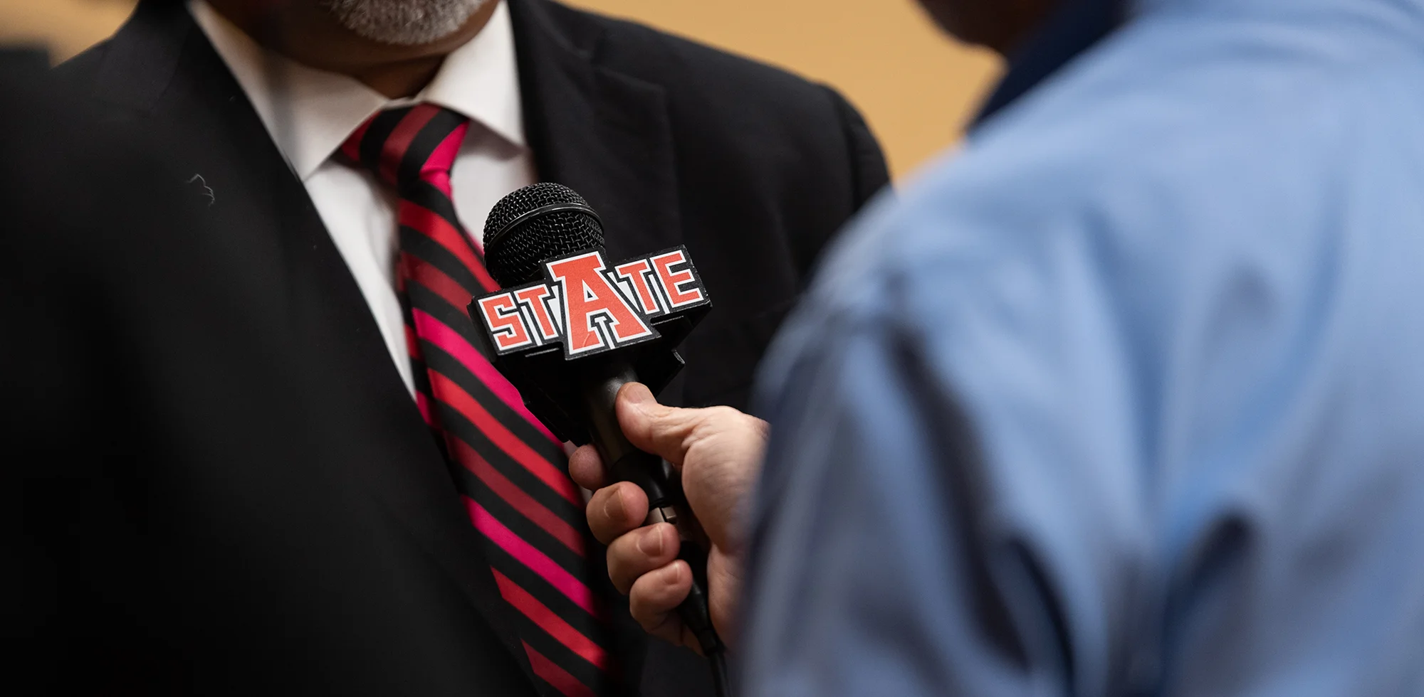 A close-up of someone holding a microphone with the A-State logo on it.