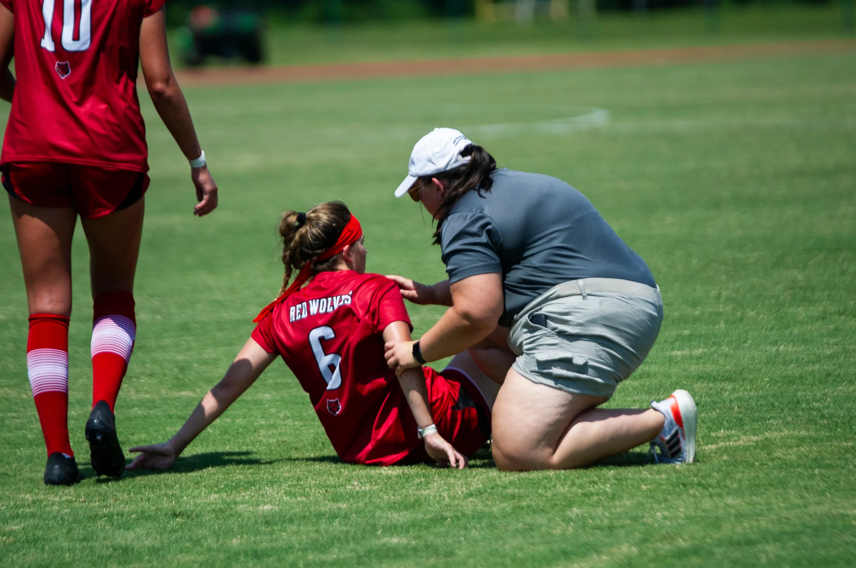 A-State soccer player on field receiving help from athletic trainer while laying on the ground with injury.