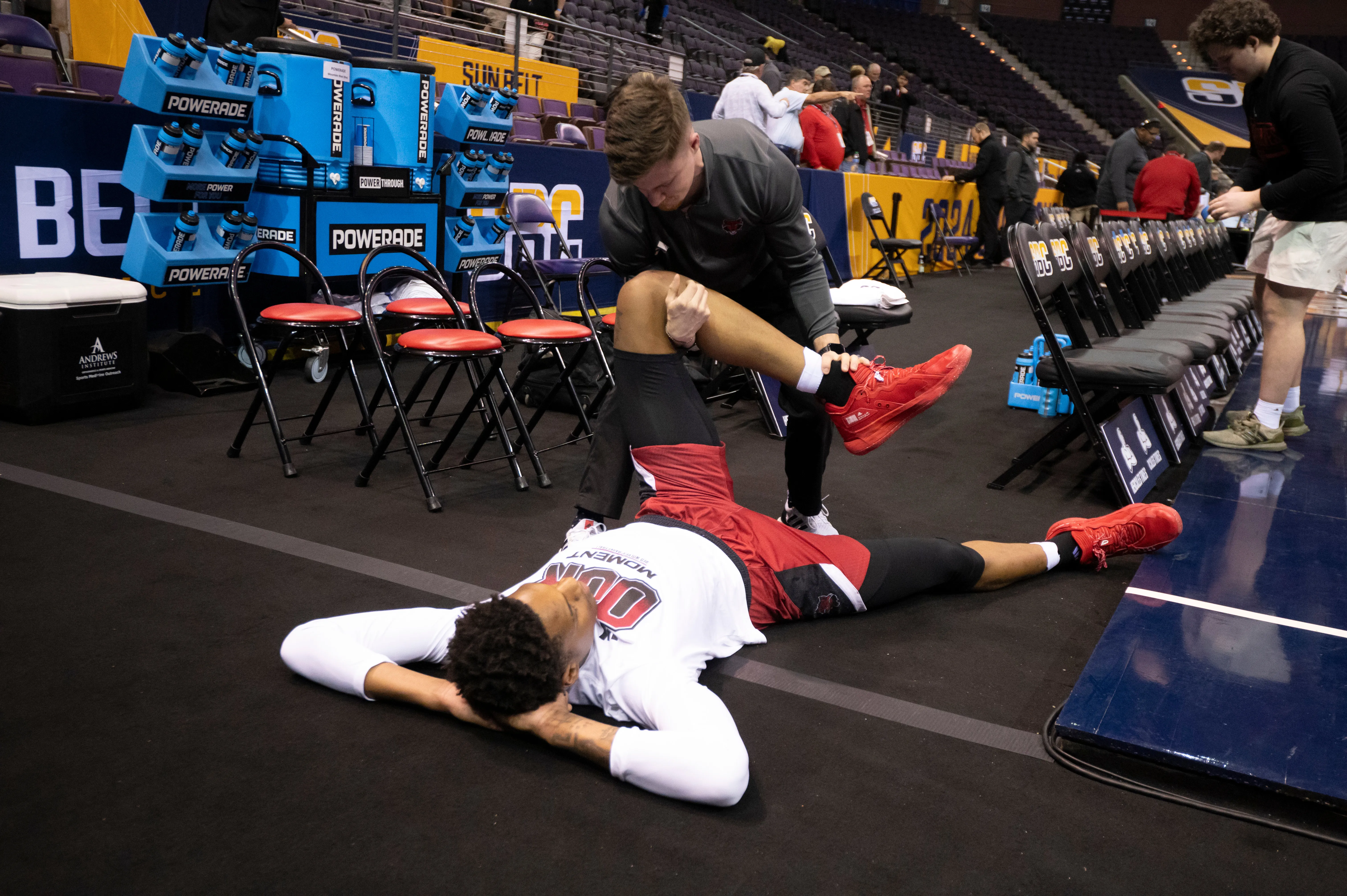 A-State athletic trainer working with basketball player on leg stretches on the court.