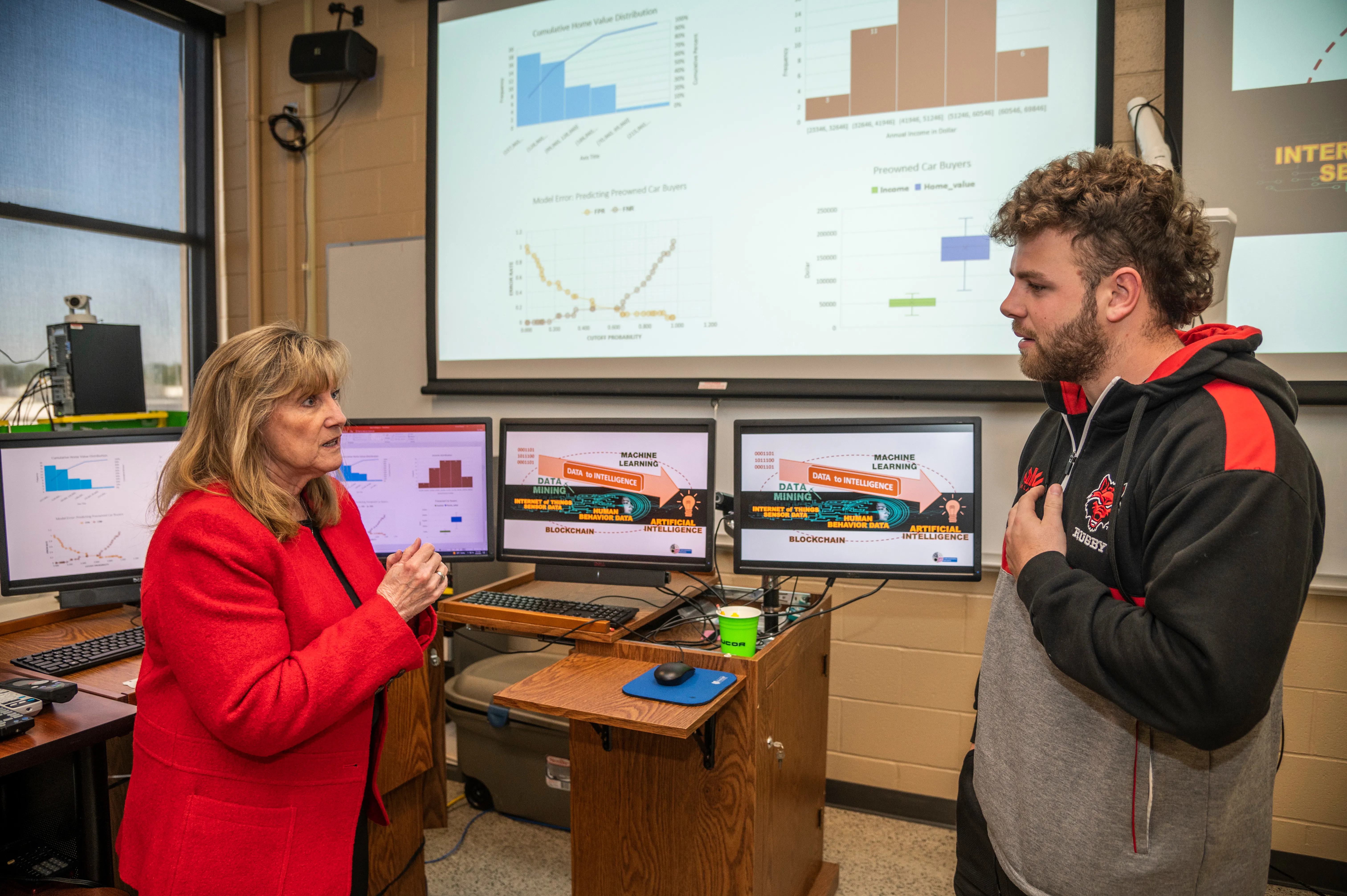 A-State business student working with teacher in front of class with notes and slides about AI and analytics behind them.