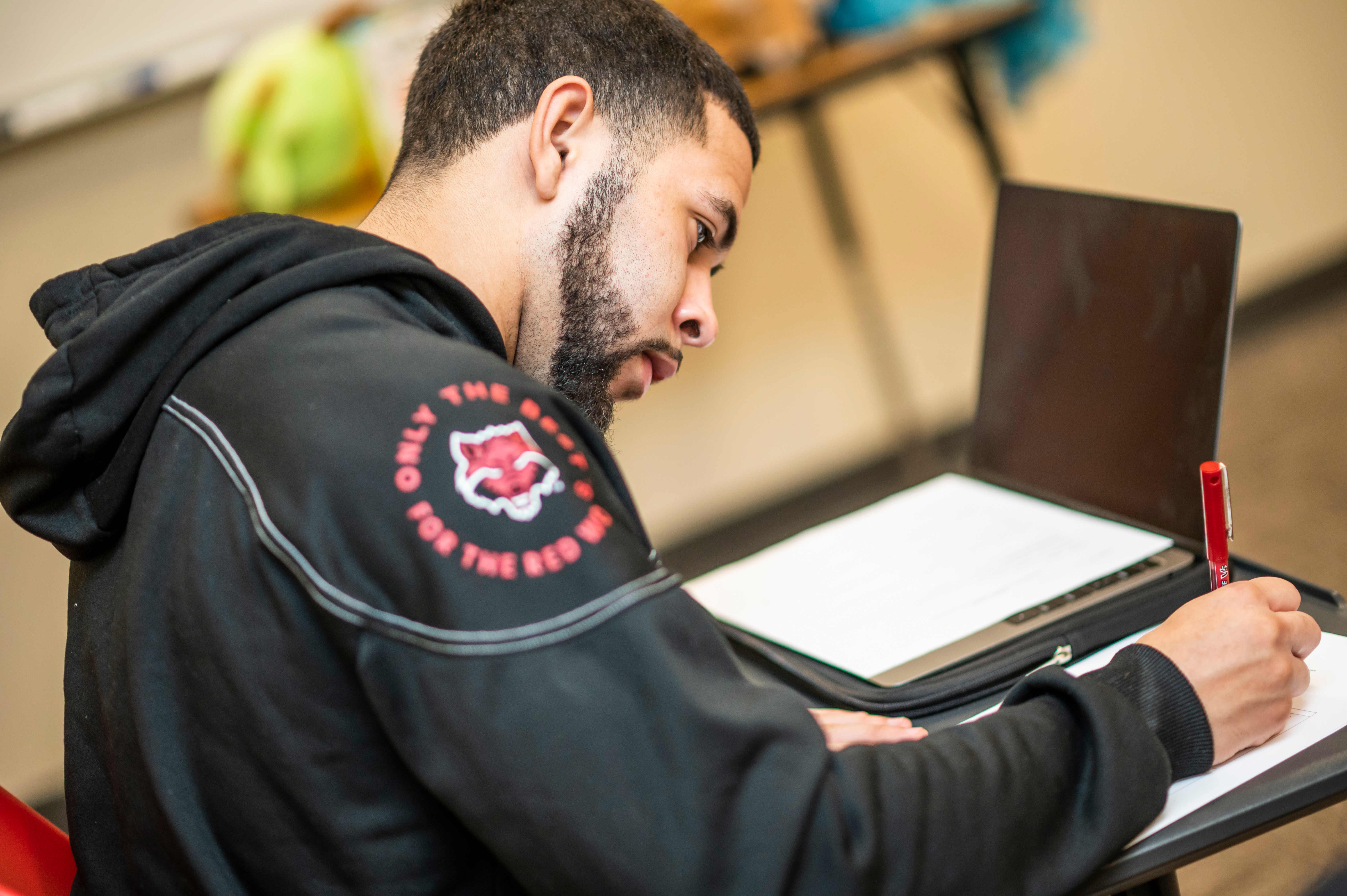 A student writing and wearing a jacket with a Red Wolf patch on the shoulder.