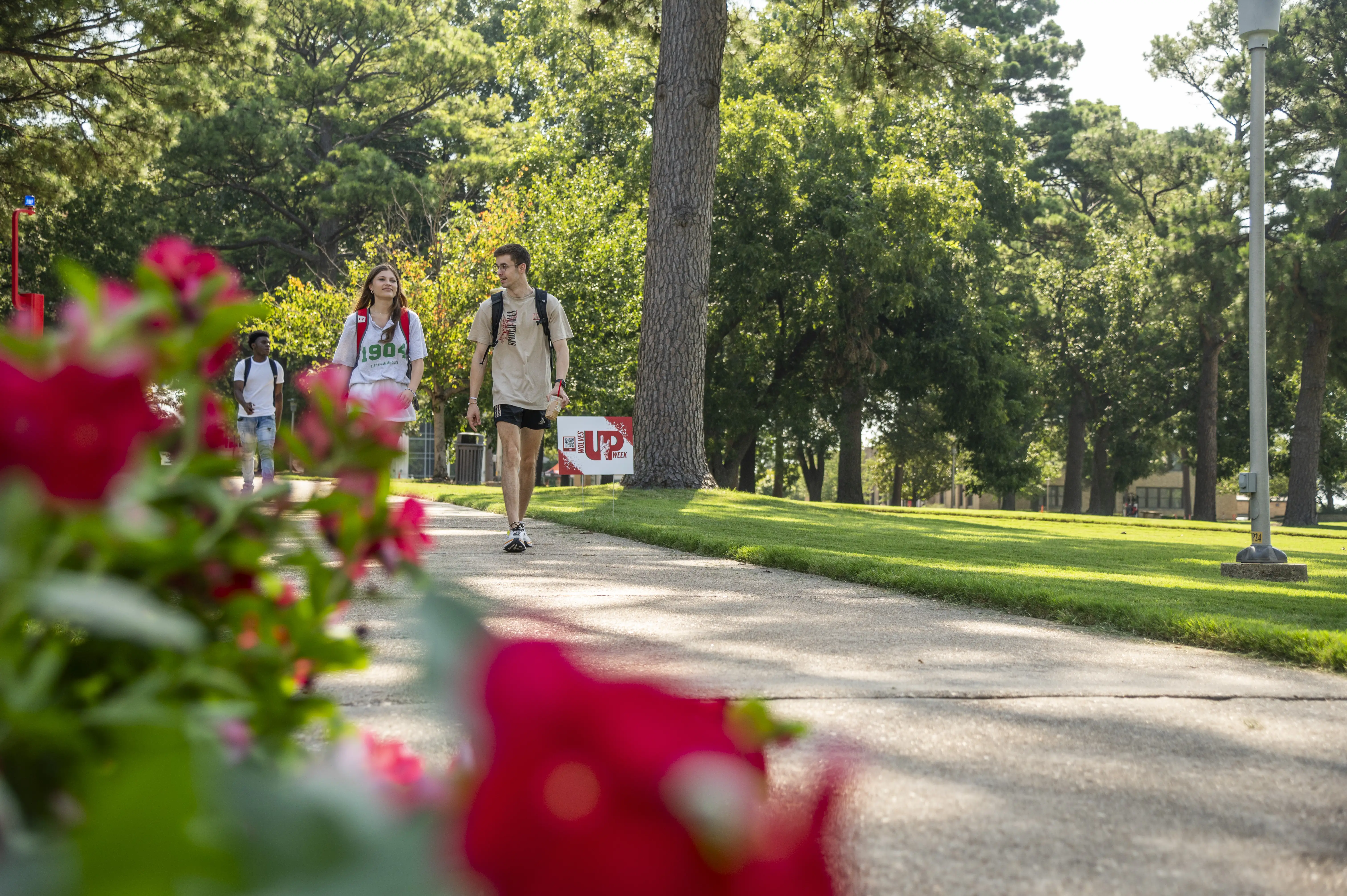 Students walking on campus, framed by red flowers.