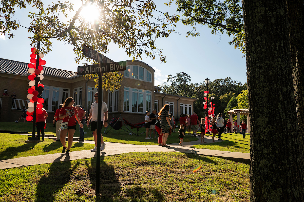 People walk past Red Wolf Blvd and Alumni Blvd signs at an A-State Alumni event.