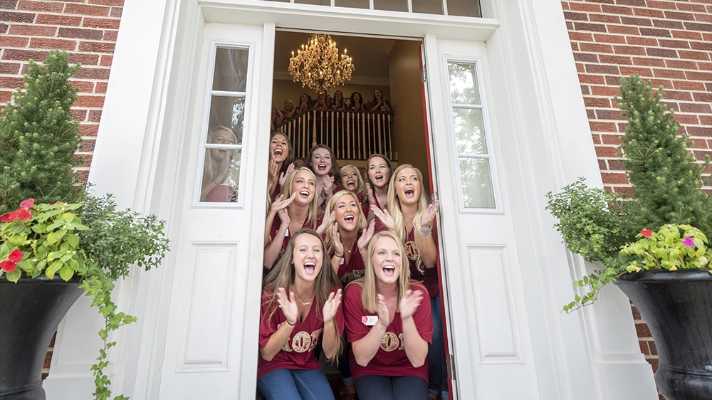 Group of individuals standing outdoors in teal shirts near white tents and colorful decorations during recruitment.