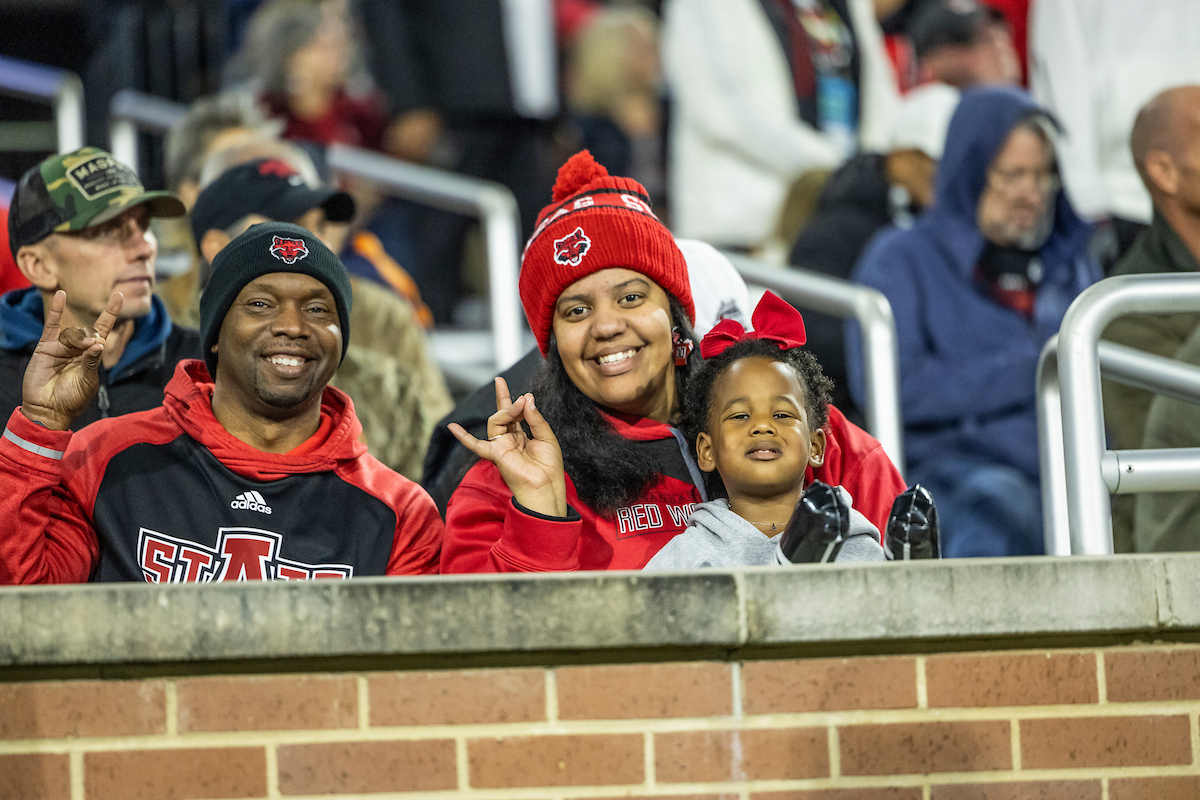 Smiling family dressed in Red Wolves gear during an Arkansas State night football game.