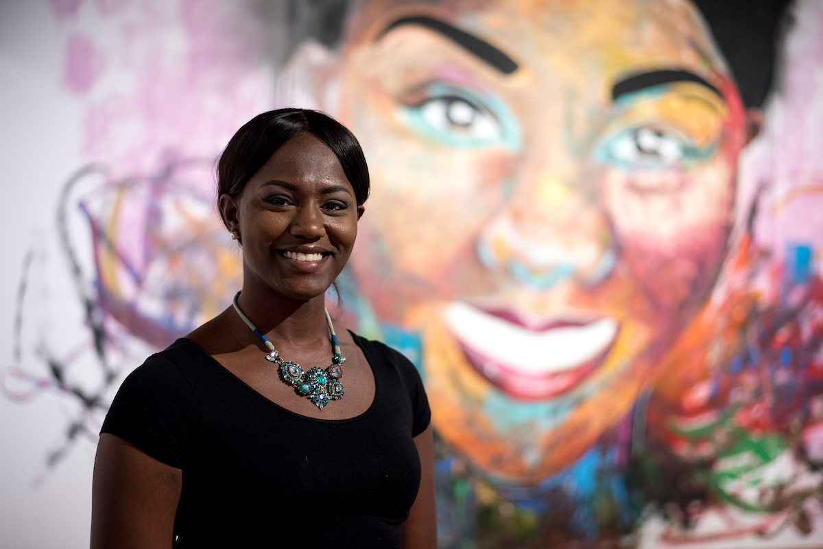 Student poses in front of a vibrant portrait painting at an A-State art exhibition.