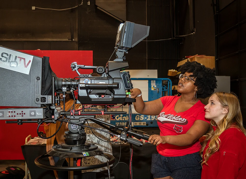 Student showing another student how to operate a camera.