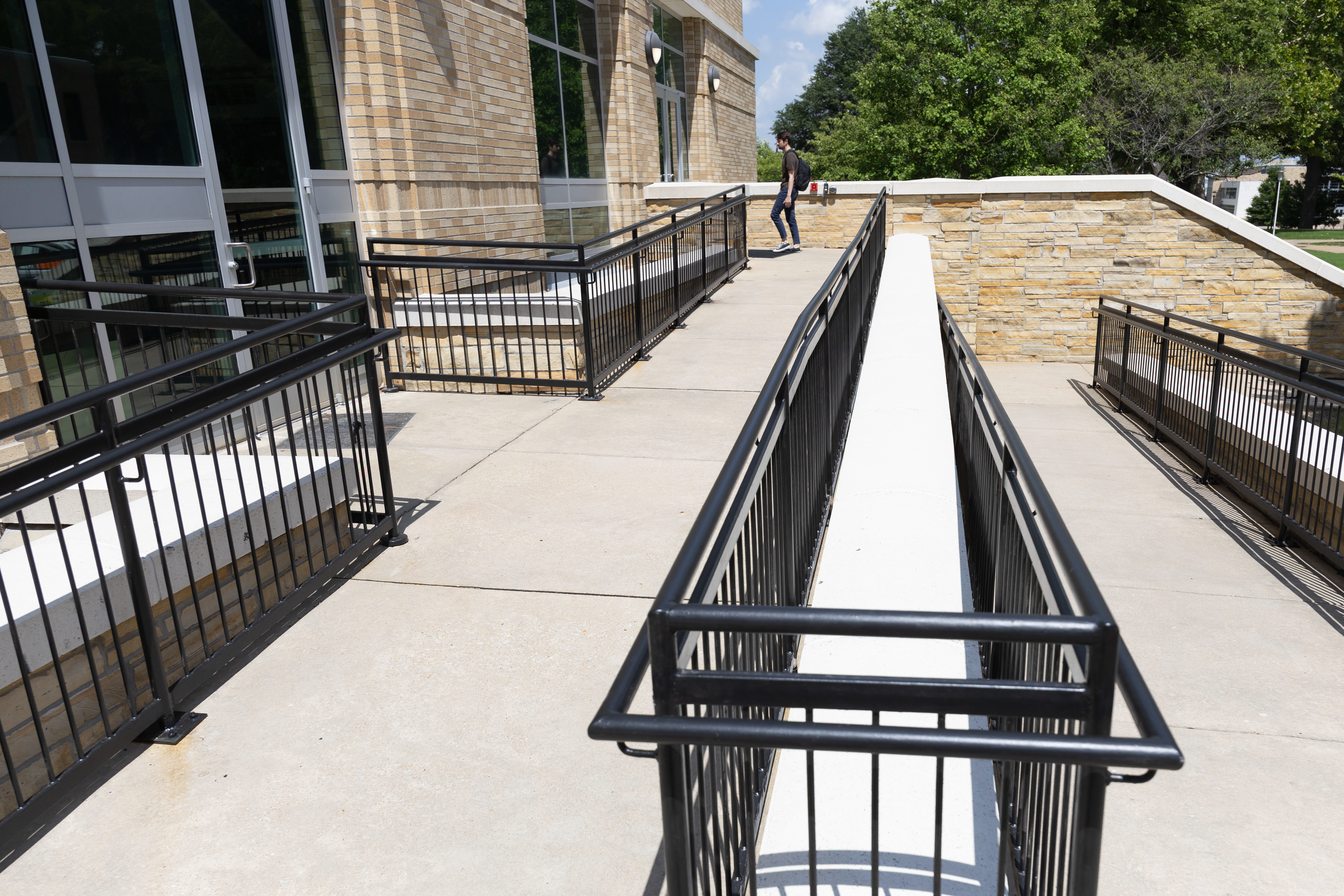 Accessibility ramp with black metal rails on campus, leading to building entrance.