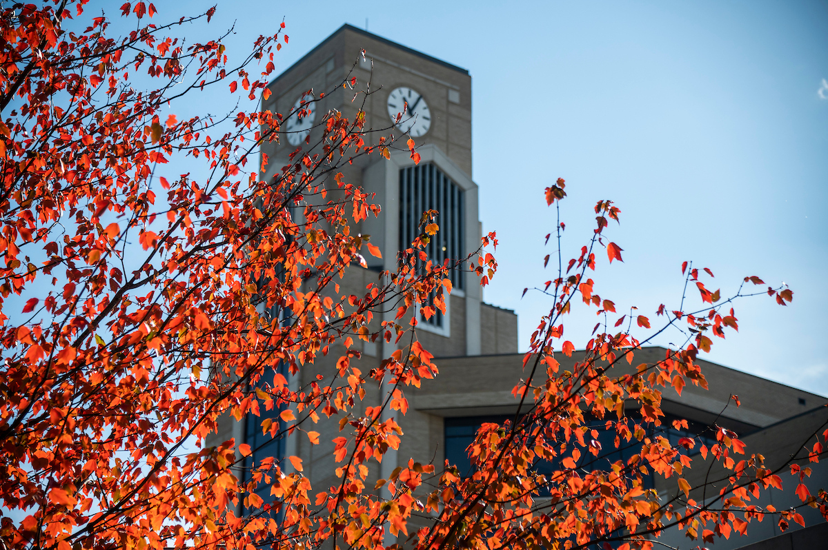 Bright red fall leaves frame the Dean B. Ellis clock tower against a clear blue sky.