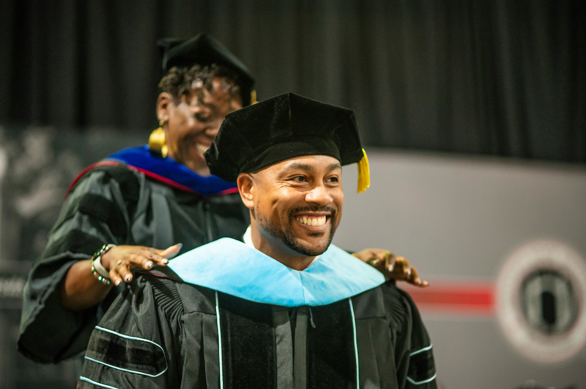 Doctoral graduate smiles while being hooded during commencement.