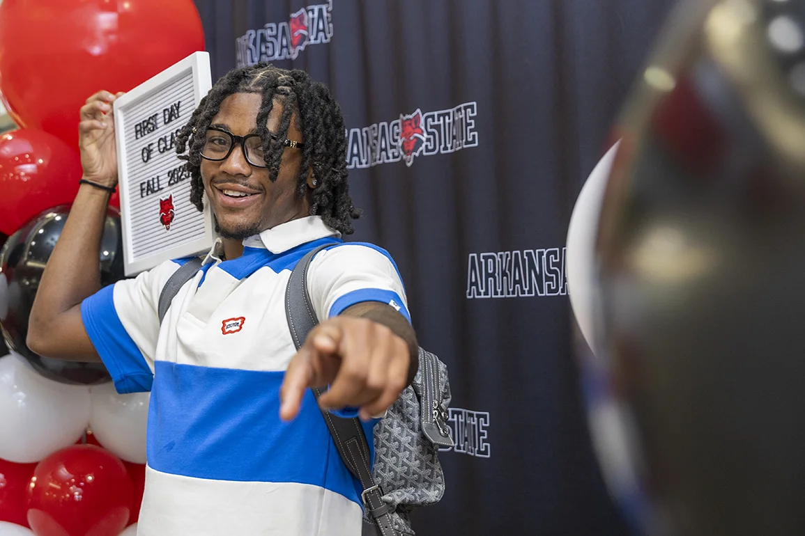 Male student with backpack excitedly pointing at camera