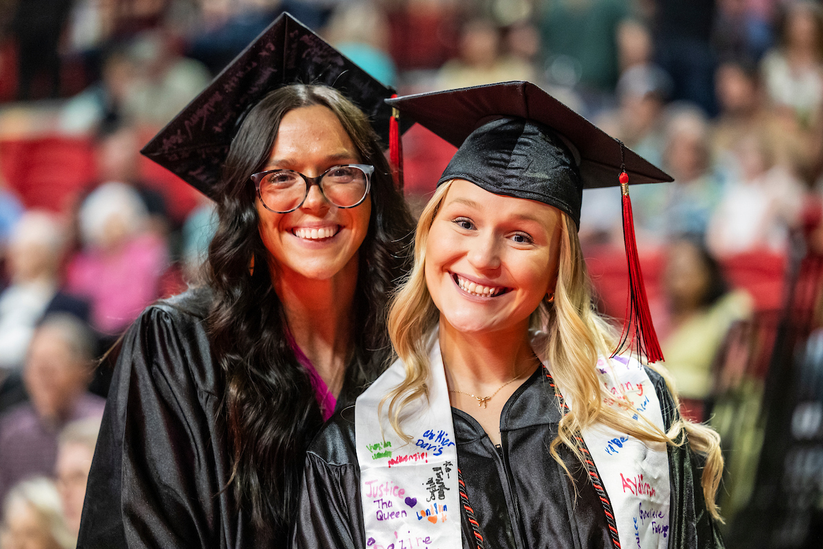 Two A-State graduates smile in caps and gowns during commencement.