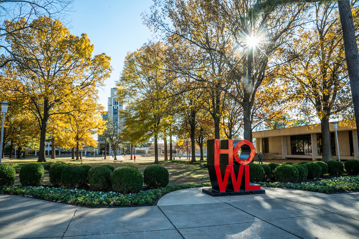 Fall sunlight shines through trees near the HOWL statue on the astate campus.