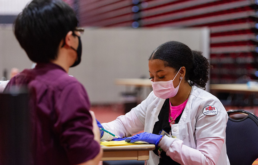 Masked A-State nursing student volunteering at a clinic.