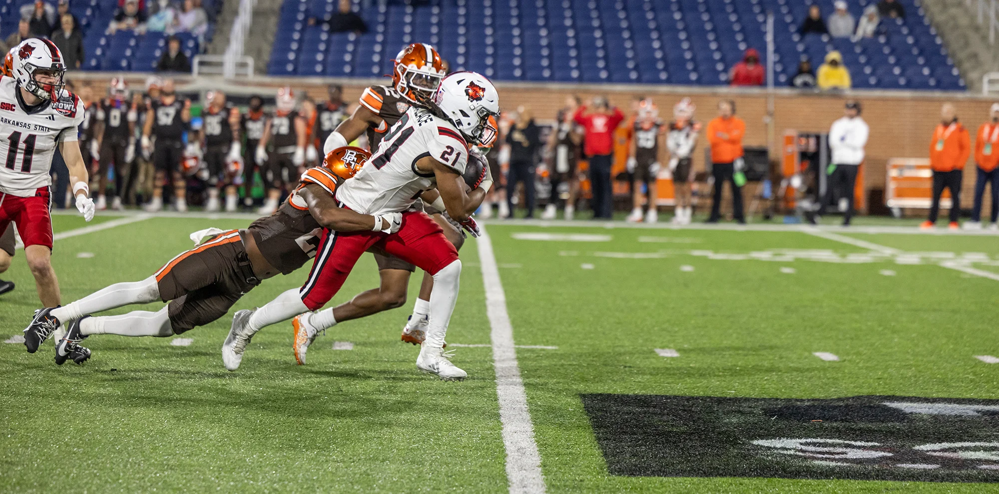 Red Wolves football player holding onto ball as other players try to tackle him
